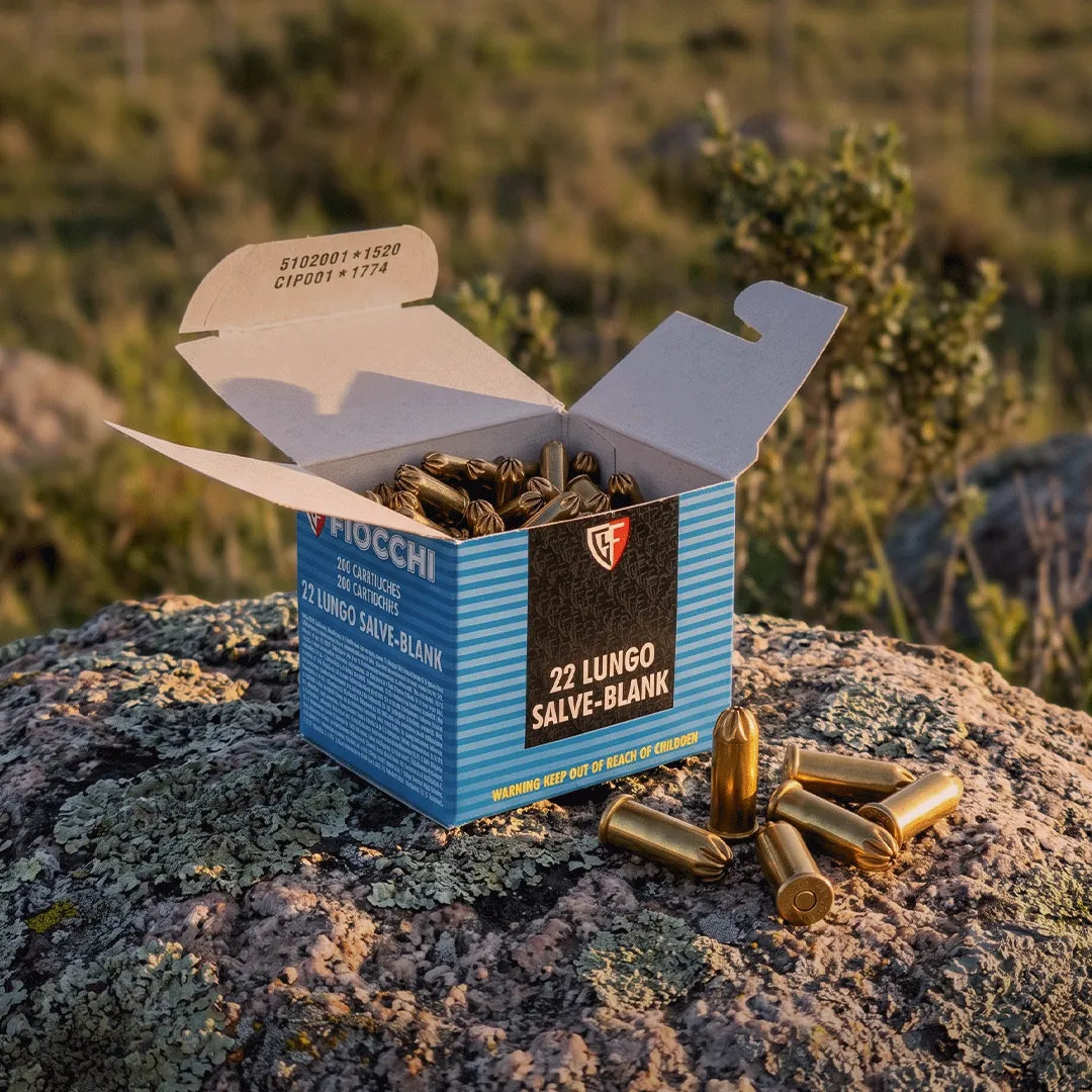 Caja abierta de balas de fogueo Fiocchi calibre .22 sobre rocas en entorno natural.